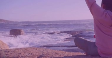 Derin nefes alan kadın, derin nefes alan dalga ikonlarıyla meditasyon yapmak için kıyıda kollarını esnetiyor. Dinginlik, farkındalık, doğal, huzur, tefekkür, açık hava, manzara.