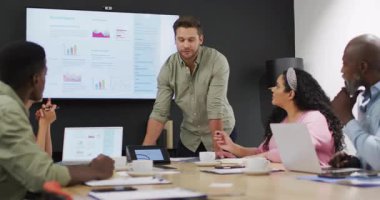 Eğik sunucu, meslektaşlarını konferans odasına çağırıyor, yıllık rapor çubuğu grafiklerini vurguluyor. Kurumsal, takım çalışması, iş, analitik, tartışma, profesyonel, liderlik