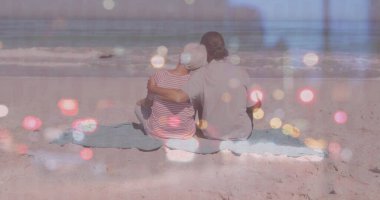 Yazlık giysiler giymiş, kumlu sahil battaniyesine yaslanmış, okyanus dalgalarına yaslanmış bir çift. Romantizm, rahatlama, dinginlik, rahatlık, yaşam tarzı, uyum, sükunet