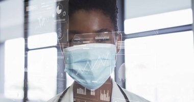 Paltolu kadın doktor, klinikteki dijital sağlık çizelgelerini maske ve steteskopla inceliyor. Tıbbi, teknoloji, profesyonel, yenilik, sağlık, modern, araştırma