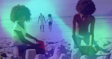 Şortlu çocuklar diz çöküp kumdan kaleler inşa ediyorlar. Kovalar, ayak izleri ve yürüyen ebeveynler. Aile, eğlence, tatil, açık hava, eğlenceli, yaz, su