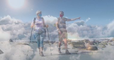 Yürüyüş kıyafetli olgun bir çift kıyıda yürüyüş direkleri kullanıyor sırt çantaları ve yüz maskeleriyle. Macera, keşif, esneklik, manzara, açık hava, refah, aktif