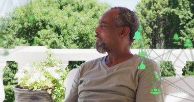 Oturan gri tişörtlü adam soldaki avluya bakıyor, çiçek açan saksı, yeşil dijital ikonlar. Açık hava, rahatlama, teknoloji, bahçıvanlık, şehir, eğlence, bağlantı