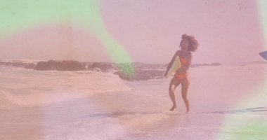 Turuncu bikinili bir kadın sahilde sörf yapmak için sarı bir badiba taşıyor. Sahil, yaz, sahil, dinlenme, rahatlama, canlı, açık hava.