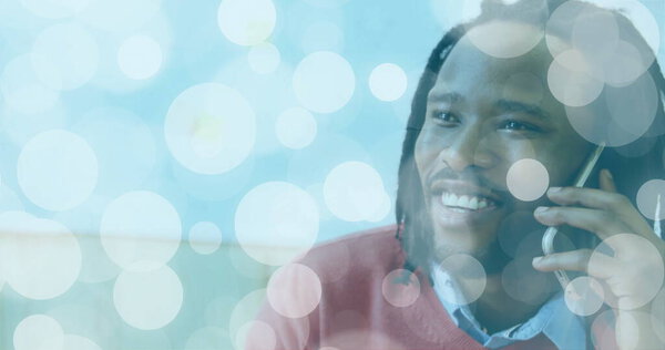 Smiling mid adult man with dreadlocks speaking into smartphone in lounge, red sweater, copy space. Professional, casual, modern, communication, connection, relaxation, leisure