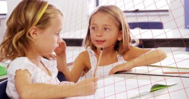 İki öğrenci yazı partnerini kalemle tıklatıyor ve sınıfta gizli fısıldaşıyorlar. İşbirliği, arkadaşlık, gençlik, öğrenme, iletişim, konsantrasyon, takım çalışması