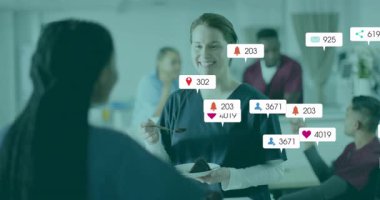 Hastane molasında pasta ısırığı sunan hemşire takımın etrafında yüzen sosyal ikonlar oluşturuyor. Sağlık, takım çalışması, dostluk, kutlama, sosyal medya, pozitif, canlı