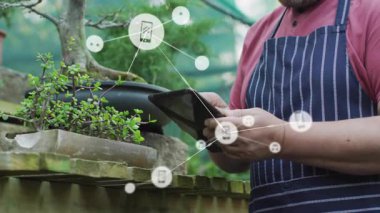 Kıdemli adam bahçedeki tableti tıklayarak bonsai 'nin etrafında büyüyen telefon ve müzik ikonları ağı oluşturuyor. Teknoloji, bahçıvanlık, bağlantı, yenilik, açık hava, yaşam tarzı, rahatlama