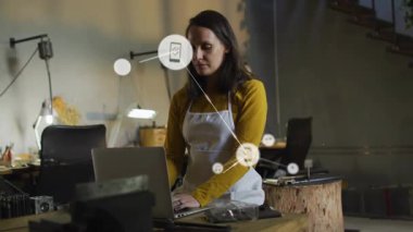 Stüdyoda bilgisayarında akıllı telefon ve müzik ikonlarıyla teknoloji ağını görselleştiren orta yaşlı bir kadın. Atölye, zanaatkar, bağlantı, dijital, el işi, yenilik, çalışma alanı