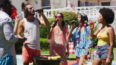 Arkadaşları havuz başında ızgara yapıyor ve sosyal tepki simgeleri yayınlarken telefonları dinliyorlar. Açık hava, boş zaman, kutlama, yaz, yaşam tarzı, hareketli, sosyal