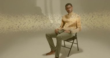 Kol saatini kontrol eden erkek model sandalyenin etrafında gezinen altın parçacıklar sergilenen teknolojiyi gösteriyor. Zarif, fütürizm, sofistike, dijital, minimalizm, düşünceli, rafine