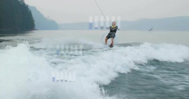 Erkek wakeboardcu uyanışı yakalıyor ve sporu oyuyor. Kontrolü sağlamak için halat çekme hareketine yöneliyor. Macera, açık hava, su eğlencesi, spor, aktivite, manzara, hareket