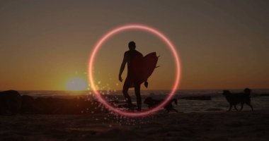 Gün batımında elinde sörf tahtası tutan erkek sörfçü. Neon yüzük ve köpeklerle. Plaj, siluet, günbatımı, sahil şeridi, macera, sükunet, doğa