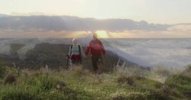 Gün batımında patikada el ele yürüyen çiftler, yürüyüş direkleri, sırt çantaları. Macera, keşif, açık hava, manzara, vahşi doğa, arkadaşlık, dayanıklılık.