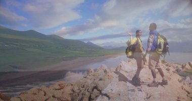 Neon yeşil sırt çantaları ve yürüyüş botlarıyla sahile tepeden bakan yürüyüşçüler, kopyalama alanı. Macera, keşif, vahşi doğa, manzara, manzara, seyahat, boş zaman