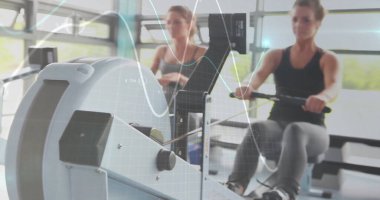 Spor salonundaki sabit makinelere dijital monitörlerle sıvı vuruşları yapan kürek çeken atletik arkadaşlar. Fitness, yoldaşlık, açık hava ilhamı, canlı, enerji, güç, eğitim