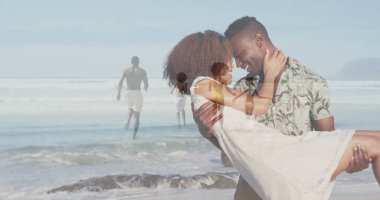 Kıyı şeridinde, üzerinde okyanus dalgaları olan beyaz elbiseli bir kadın taşıyan, çiçekli gömlek giyen bir kaldırıcı. Romantizm, çift, açık hava, eğlence, coşku, manzara, arkadaşlık.