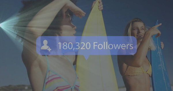 Держащие доски для сёрфинга, женщины в полосатых и жёлтых бикини на пляже, с накладываемым количеством последователей. Пляж, лето, дружба, мода, оживление, отдых на открытом воздухе