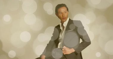 Erkek model taburede kayıyor ve koyu renk takım elbiseyi moda fotoğrafçılığıyla örtüyor. Şık, zarif, sofistike, minimalist, profesyonel, çevresel, düşünceli.