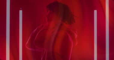 Beyaz borularla çevrili kırmızı ışıkta dönen kapüşonlu erkek. Portre, moda, dinamik, çağdaş, ruh hali, sinema, stüdyo