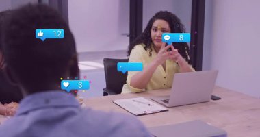 Sarı bluz sunucusu konuşuyor. İş arkadaşı konuşurken sosyal medya simgelerinin yükseldiğini gösteriyor. Takım, işbirliği, dijital, profesyonel, ağ, iletişim, analiz