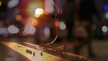 Klavyede açılış akoru çalan kadın müzisyen gece müziği için Bokeh ışıkları arasında melodi şekillendiriyor. Enstrüman, gececilik, ambians, dinginlik, performans, kentsel sanatçılık