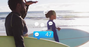 Kumlu sahil şeridinde duran iki sörfçü gözleri gölgeliyor ve sörf tahtalarını sürüklüyor, dalgıç kıyafetleri giyiyor. Macera, yaşam tarzı, minimalizm, kıyı, aktivite, uyum, açık hava