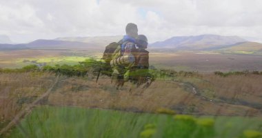 Otlu yamaçtan vadiye bakan sırt çantalı ve hasırlı iki yürüyüşçü. Macera, keşif, manzara, yürüyüş, vahşi doğa, doğa.