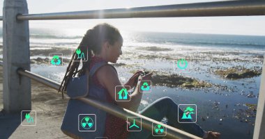 Deniz kenarındaki korkuluklara yaslanmış sırt çantalı, elinde telefon taşıyan, ekolojik simgelerle oturan bir kadın. Sürdürülebilirlik, koruma, dijital, kentsel, dinginlik, çevre dostu, modern