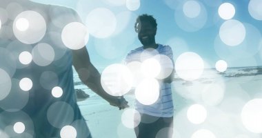 Kumsalda el ele tutuşan, günlük plaj kıyafetleri giyen, dairesel ışıklı bir çift. Romantik, açık havada, sakin, enerjik, genç, doğal, deniz kenarında