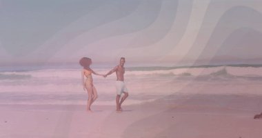 Sarı bikinili ve açık yüzme şortlu, kumlu kıyı şeridi boyunca el ele tutuşan yürüyen plaj çifti. Romantizm, eğlence, açık hava, macera, sükunet, uyum, tatil