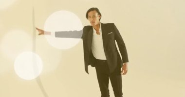 Model, sürüklenen ışık kürelerine tepki veriyor. Moda reklamı için bej arka planda kollarını kaldırıyor. Soyut, zarif, sofistike, aydınlatma, sinematik, minimalizm, profesyonellik