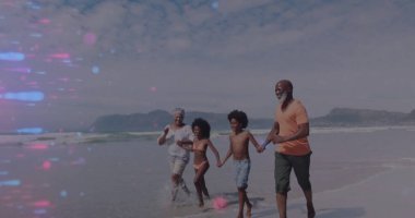 Yürüyen aile el ele tutuşuyor ve kumsaldaki ıslak kumda su sıçratıyor, mayolarla. Aile, kıyı şeridi, su, eğlence, açık hava, rahatlama, birliktelik.