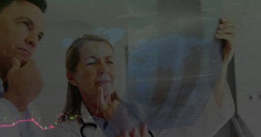 Üst düzey kadın ve olgun erkek doktorlar steteskopla röntgen filmini inceliyor. Tıbbi, sağlık, tanı, klinik, profesyonel, analiz, işbirliği