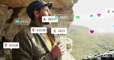 Şapka takan yürüyüşçü, kayalık tepede arazi ceketi giyen, elinde matara ve dijital kaplama simgeleri tutan. Macera, keşif, teknoloji, açık hava, panoramik, esneklik, vahşi doğa.