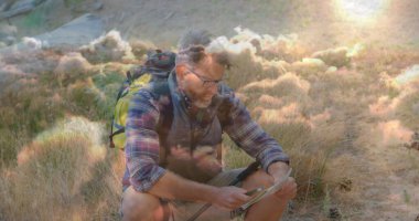 Yürüyüş yapan biri ekose gömlek giyer, güneşli çayırlarda tableti inceler, yürüyüş direği ve sırt çantasıyla gezer. Macera, keşif, açık hava, engebeli, teknoloji, vahşi yaşam, canlılık