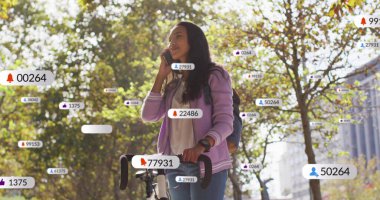 Parkta bisikletinin yanında kapüşonlu kapüşonlu giyen akıllı telefondan konuşan, uyarı simgeleriyle. Kentsel, gündelik, canlı, fitness, teknoloji, yaşam tarzı, doğa