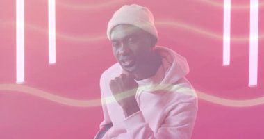 Beyaz bereli bir adam dizine vuruyor ve konuşuyor. Pembe arka planda neon dalgaların canlanmasına neden oluyor. Portre, stüdyo, modern, eğlence, iletişim, anlamlı, canlı