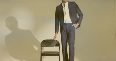 Stüdyoda sandalye arkası koltuğa el koymak ve duruşunu değiştirmek, kurumsal duruş sergilemek. Profesyonel, portre, minimalist, resmi, kendine güvenen, zarafet, stüdyo