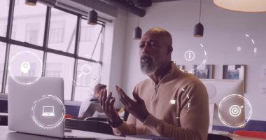 Açık ofiste dizüstü bilgisayara el kol hareketi yapan, yüzen teknoloji simgelerine sebep olan ve not alan bir danışman. İşbirliği, yenilik, üretkenlik, dijital, çalışma alanı, takım çalışması, modern