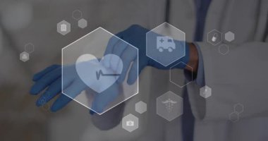 Kıdemli doktor hasta hazırlıkları sırasında mavi lateks eldivenleri açıyor ve yüzen sağlık simgelerini aktifleştiriyor. Tıbbi, sağlık, profesyonel, klinik, tanı, dijital, kısır