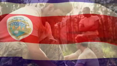 Duran asker askeri eğitim talimatları veriyor, diz çökmüş asker vites kayışlarını bağlıyor. Askeri, takım çalışması, kamuflaj, açık hava, eğitim, yoldaşlık, taktik