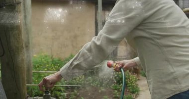 Bahçıvan musluğu kavrayıp kıvırıyor, çiçekleri suluyor ve canlandırılmış damlacıklar kıvrılıyor. Bahçıvanlık, açık hava, doğa, yeşillik, ekolojik, çevre dostu, besleyici