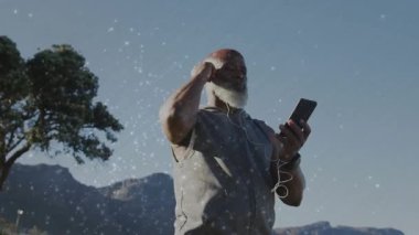 Kulaklık takan adam telefonu dağ tepesinde tutuyor, kabloyu ayarlıyor, teknolojiyi akıtmadan önce. Macera, rahatlama, doğa, açık hava, teknoloji, sükunet, keşif