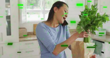 Yetişkin Koreli kadın bakkaliyeyi boşaltırken çağrıyı ikili kod olarak dengeleyerek yoğunlaşıyor. Teknoloji, dijital bozulma, ev, çoklu görev, modern, yaşam tarzı, elektronik