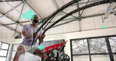 Spor salonundaki savaş halatlarını kaldıran ve spor yapmak için canlandırılmış yeşil bulut simgelerini aktif hale getiren adam. Spor, güç, dayanıklılık, eğitim, hareket, enerji, teknoloji