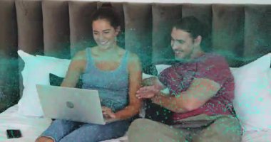 Çift yatakta dizüstü bilgisayarı yerleştirip birlikte yazarken partnerleri de turkuaz kaplama darbelerini işaret ediyor. Romantizm, samimiyet, bağlantı, eğlence, modern, konfor, dijital