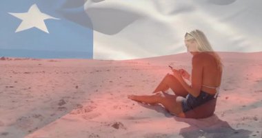 Plajda süzülerek yürüyen bir kadın arkada dalgalanan şeffaf bayrak projeksiyonu için akıllı telefon kaldırıyor. Deniz kenarı, dinlenme, sükunet, minimalist, yaşam tarzı, iletişim, yaz