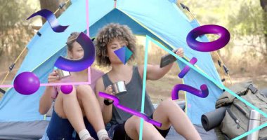 İki kadın kamp alanında bardak tutuyor. Bir tanesi, soyut çadır şekillerinin arasında akıllı telefon çerçeveli selfie çekiyor. Macera, dostluk, açık hava, coşku, doğa, rahatlık, rahatlama.