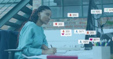 Bir kadın not yazıyor ve uyarıları izliyor. Artan sosyal medya ölçümlerini takip ediyor. Yaratıcı, üretkenlik, modern, çalışma alanı, yansıma, dijital, yenilik